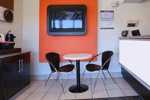 Un pequeño comedor con una mesa redonda y dos sillas, un televisor en la pared y un mostrador con una caja registradora.