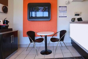 Un pequeño comedor con una mesa redonda y dos sillas, un televisor en la pared y un mostrador con una caja registradora.