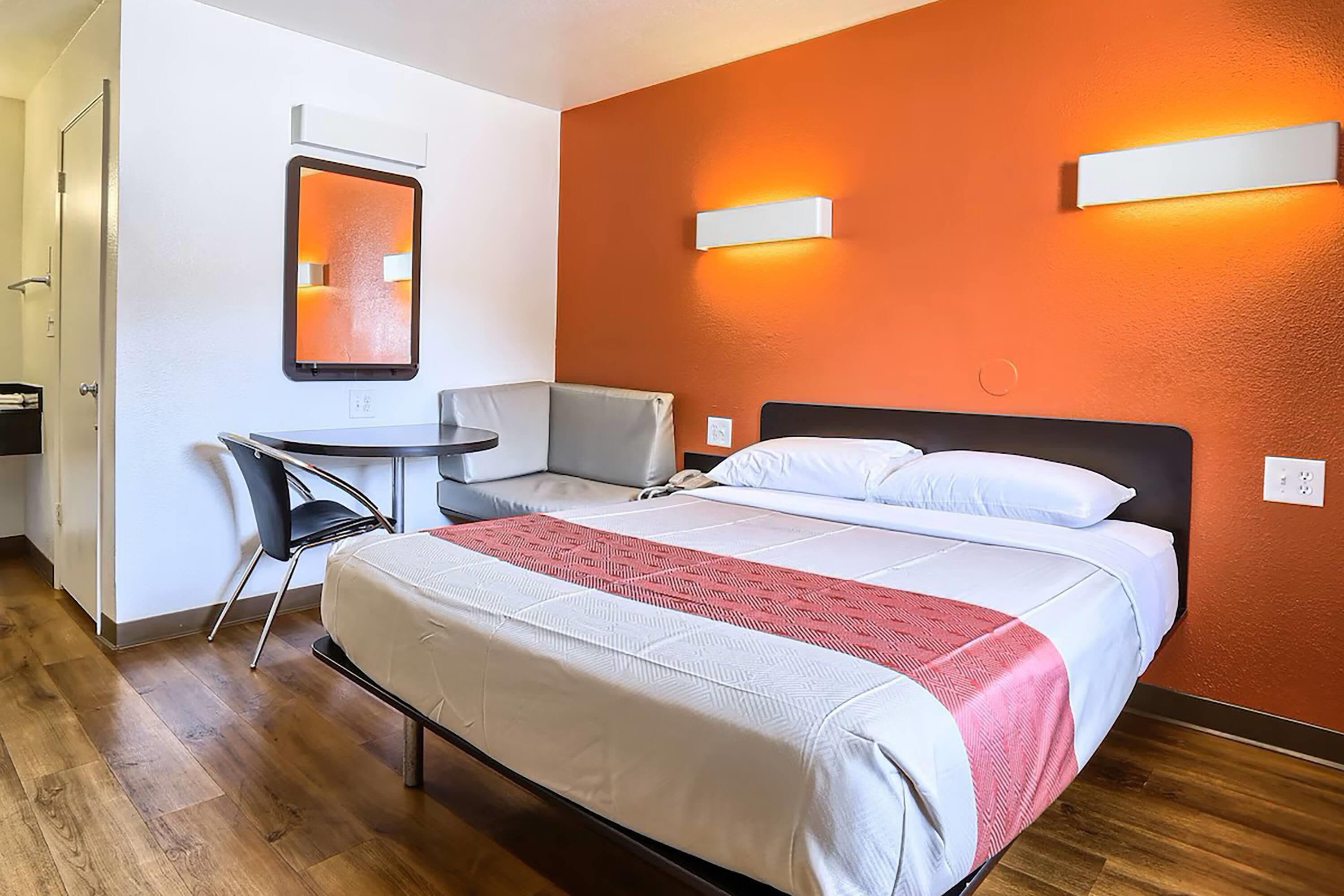 A hotel room with a bed, a desk, a chair, and a mirror.