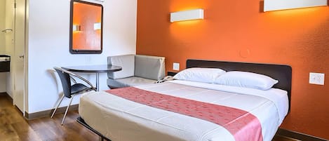 A hotel room with a bed, a desk, a chair, and a mirror.