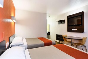 Habitación de hotel con dos camas, televisor, una mesita con sillas y televisor montado en la pared.