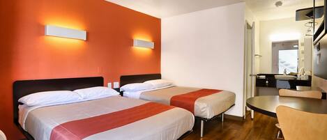 Una habitación de hotel con dos camas, una mesa de comedor y una kitchenette.