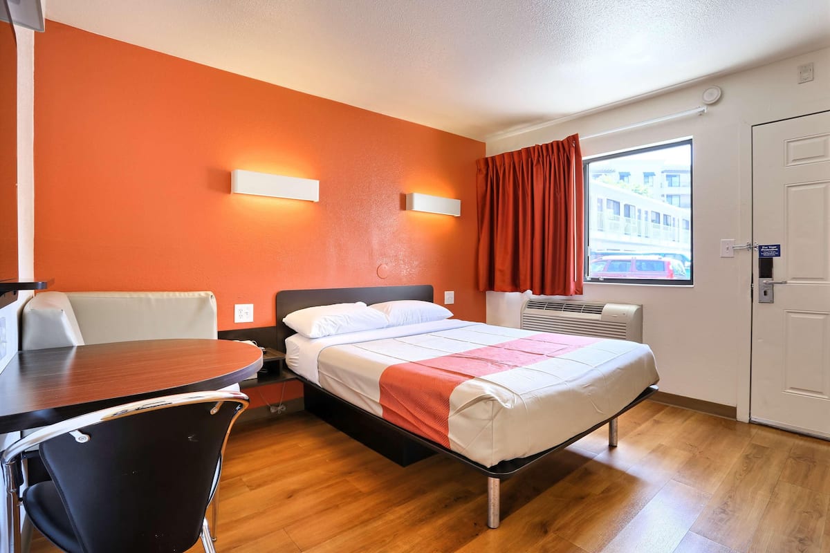 Habitación de hotel con cama, una mesa, una silla, ventana con cortinas y aire acondicionado.