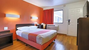Habitación de hotel con cama, mesita de noche, luz empotrada en la pared, ventana con cortinas y una puerta.