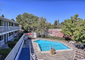 Un hotel con piscina, mobiliario exterior y vistas a árboles y un muro de ladrillo rojo.
