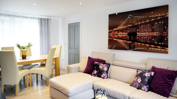 A modern living room with a sofa, a dining table with chairs, and a large framed picture of a bridge at night. - Strelley House 2, off-street parking, Perfect for Family & Contractor friendly (Nottingham)