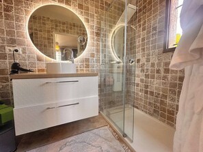A bathroom with a glass-enclosed shower, a white vanity with a round mirror, and a tiled wall. - The Room Gallery - Escappart (Tourrettes-sur-Loup)