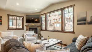 A living room with a fireplace, large windows, and a television. - Hot Tub | Ping Pong Table | EV Charger (Mammoth Lakes)