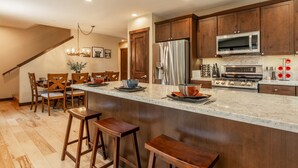 A kitchen with wooden cabinets, a stainless steel refrigerator, a microwave, and a stove. There is a bar area with stools and a dining table with chairs. - Hot Tub | Ping Pong Table | EV Charger (Mammoth Lakes)
