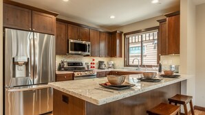 A modern kitchen with stainless steel appliances, wooden cabinets, and a large island with stools. - Hot Tub | Ping Pong Table | EV Charger (Mammoth Lakes)