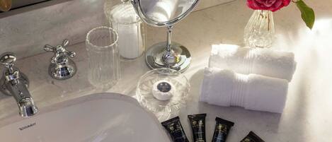 A bathroom vanity with a mirror, toiletries, and a vase with a rose.