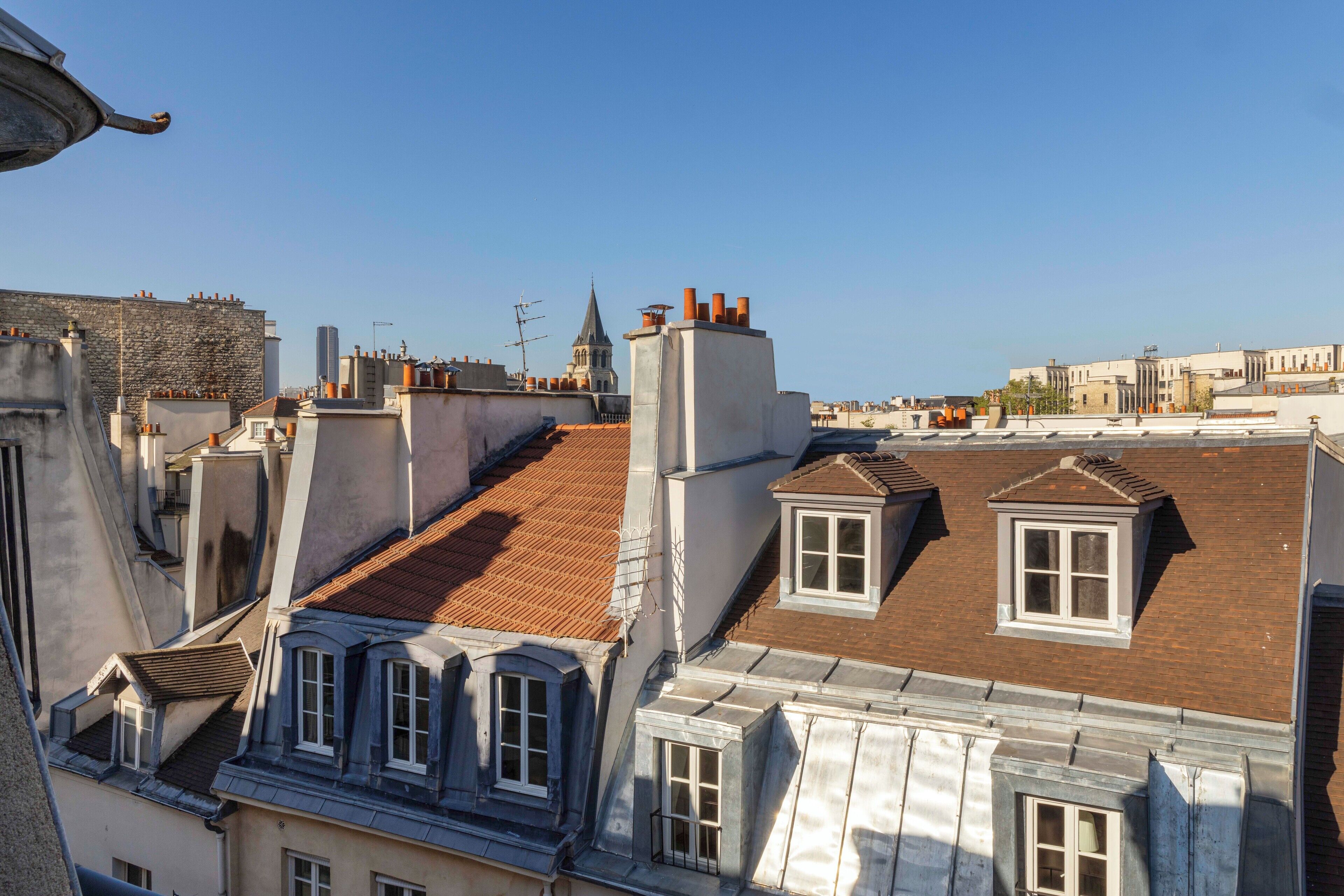 Vista des del terrat d'un edifici amb diverses xemeneies, una agulla d'església a la distància i una combinació d'estils arquitectònics.