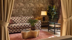 A cozy living room with a patterned sofa, a woven coffee table, a potted plant, and a chair. - Hôtel Aubépine (Paris)