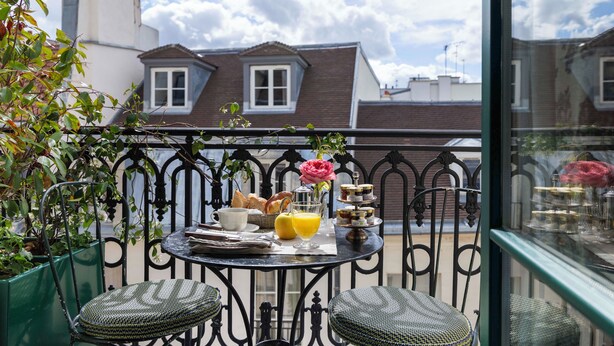 A balcony with a table set for breakfast, including bread, pastries, and a flower vase. - Hôtel Aubépine (Paris)