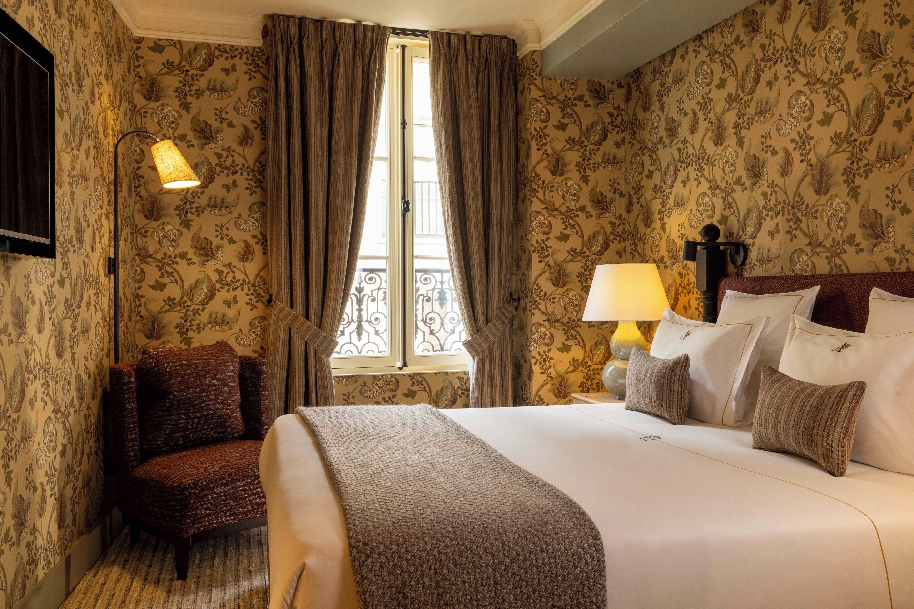 A hotel room with a large bed, a chair, a window with curtains, and a lamp.