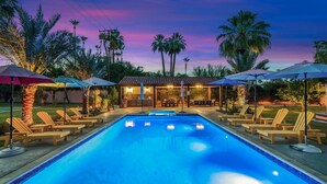 A swimming pool with lounge chairs and umbrellas, surrounded by palm trees and a bar area.