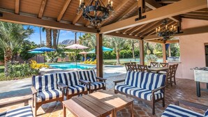 An outdoor patio with striped lounge chairs and a table, a pool, and umbrellas in the background.