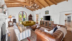 A spacious living room with a high wooden ceiling, a large arched window, a television, and a fireplace.