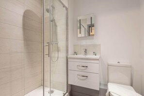 A modern bathroom with a glass shower enclosure, a white sink with a mirror above it, and a toilet.