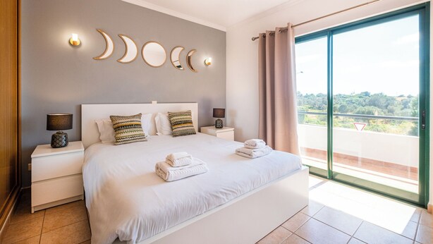 Une chambre moderne avec un grand lit, deux tables de chevet avec des lampes, une décoration murale en forme de croissant de lune et un balcon avec vue.