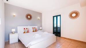 Une chambre d’hôtel moderne avec un grand lit, deux tables de chevet, des appliques murales décoratives et une vue sur l’extérieur, visible à travers une porte vitrée.