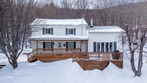 Una casa de dos pisos con terraza de madera y un paisaje cubierto de nieve.