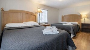 Habitación de hotel con dos camas, cada una con cabecero de madera, una ventana con persianas y una lámpara de noche.