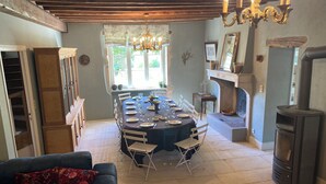 A dining area with a round table set for six, a fireplace, and a wood-burning stove. - 19th century manor house "la belle vie" 14/15 persons 5 min from Beaune (Tailly)
