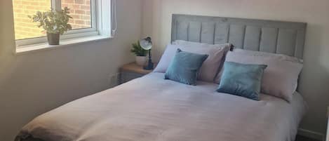 A bedroom with a bed, a nightstand, a lamp, and a window with a plant.
