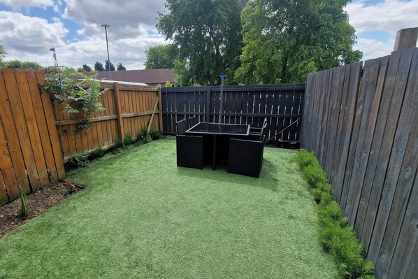Un patio trasero con césped artificial, una valla de madera y una mesa.