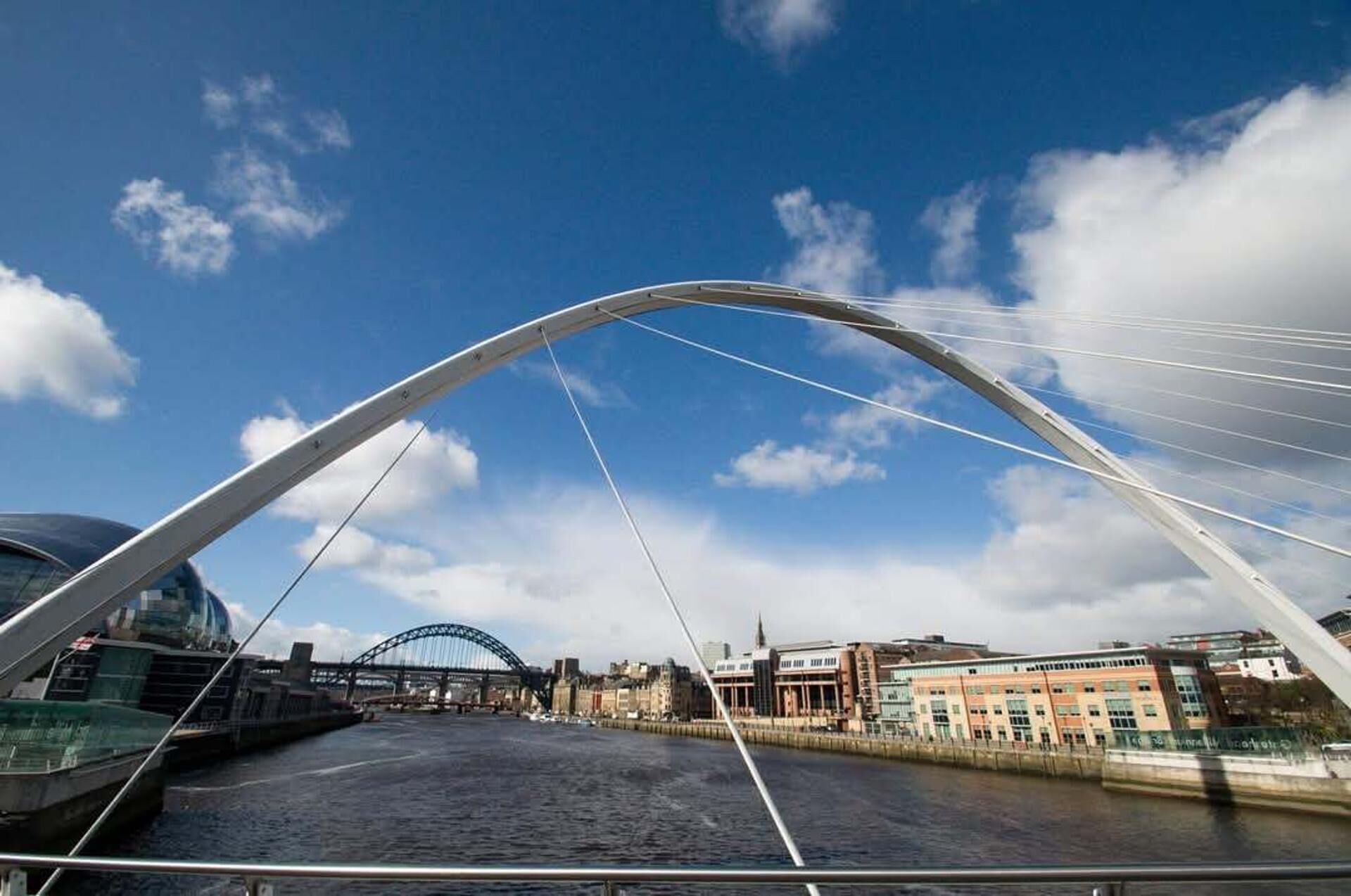 A modern bridge with a curved design, a river below, and buildings in the background.