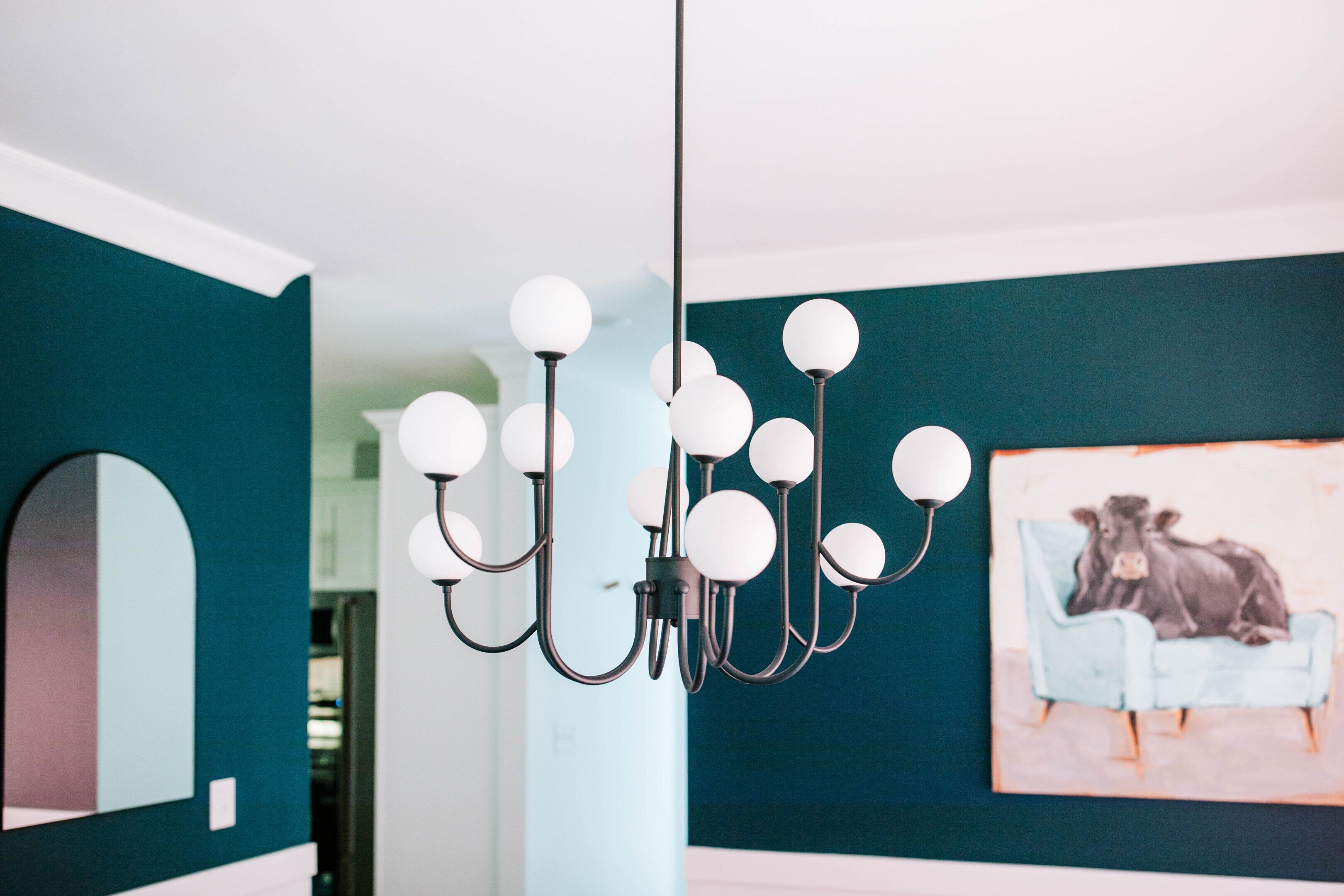A modern interior with a chandelier, teal walls, and a painting of a cow on a chair.