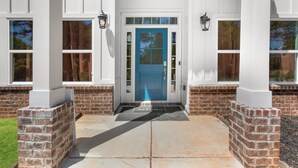 A white building with a blue door, brick columns, and a welcome mat.