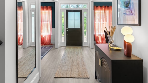 A hallway with a door, a rug, a cabinet with a lamp, and a framed picture on the wall.