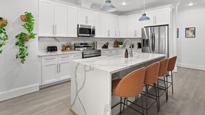A modern kitchen with white cabinets, stainless steel appliances, a marble island, and bar stools.