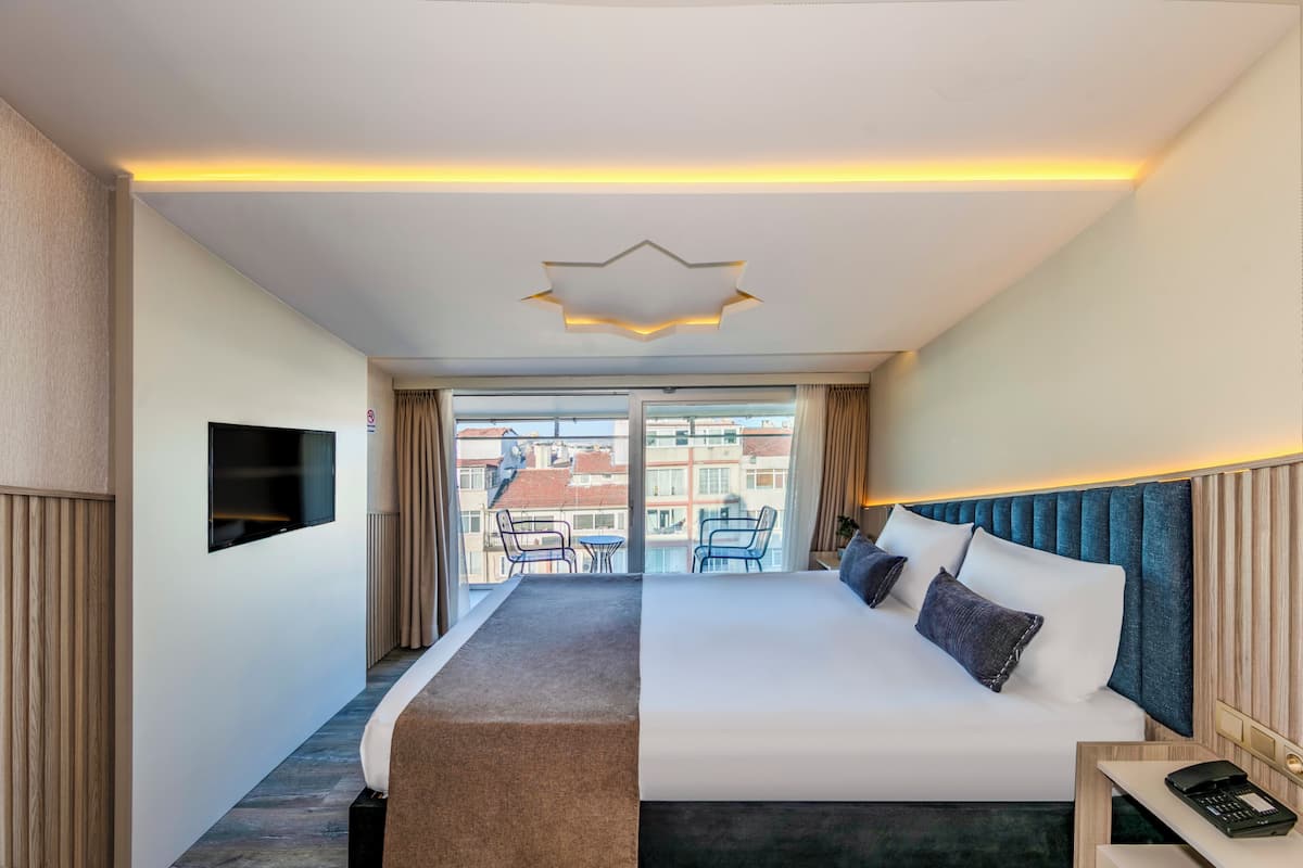 Un cuarto de hotel con una cama grande, un escritorio con teléfono, un televisor en la pared y un balcón con vista a la ciudad.