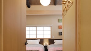 A narrow hallway leading to a room with two beds, a window, and a ceiling light.