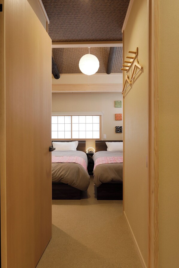A narrow hallway leading to a room with two beds, a window, and a ceiling light. - Kiyomizu & Gion Area | 2BR/2BA Kyoto Machiya + Private Maki Bath (Kyoto)