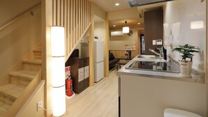 A modern kitchen with a built-in stove, a sink, and a refrigerator. There is a wooden staircase with a railing and a fire extinguisher on the wall.