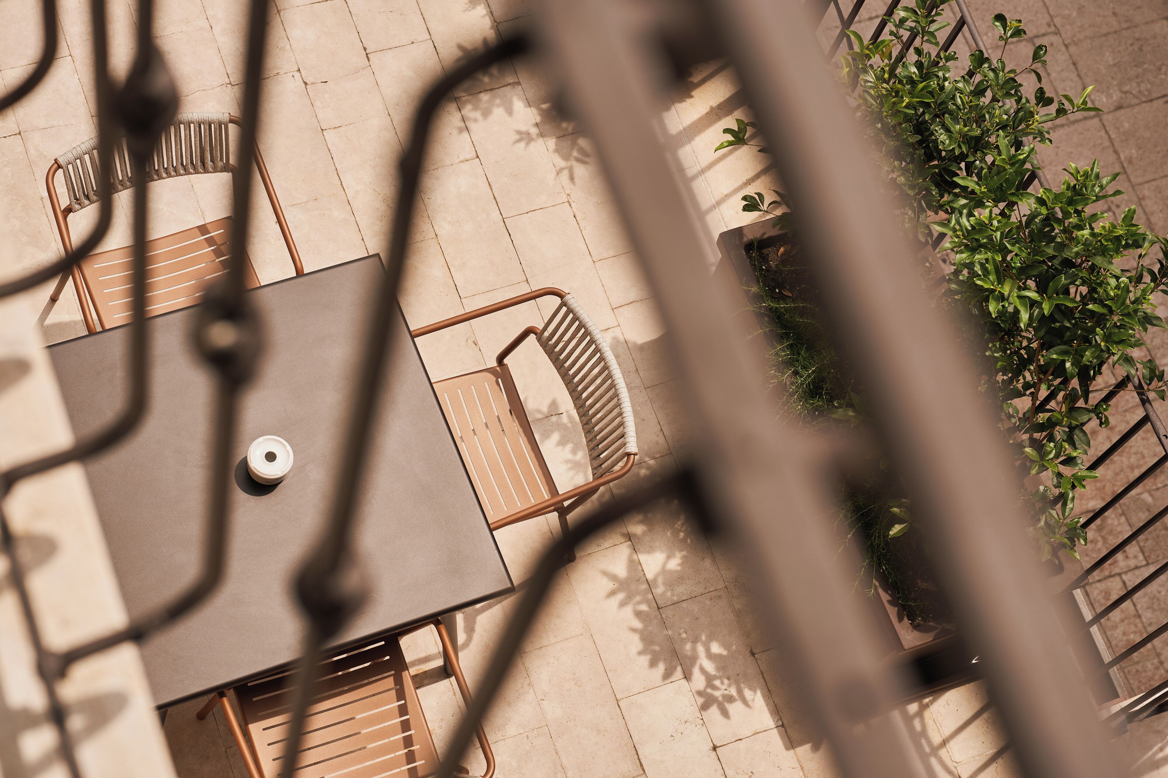 An outdoor patio area with a table and chairs, surrounded by potted plants and a metal railing.