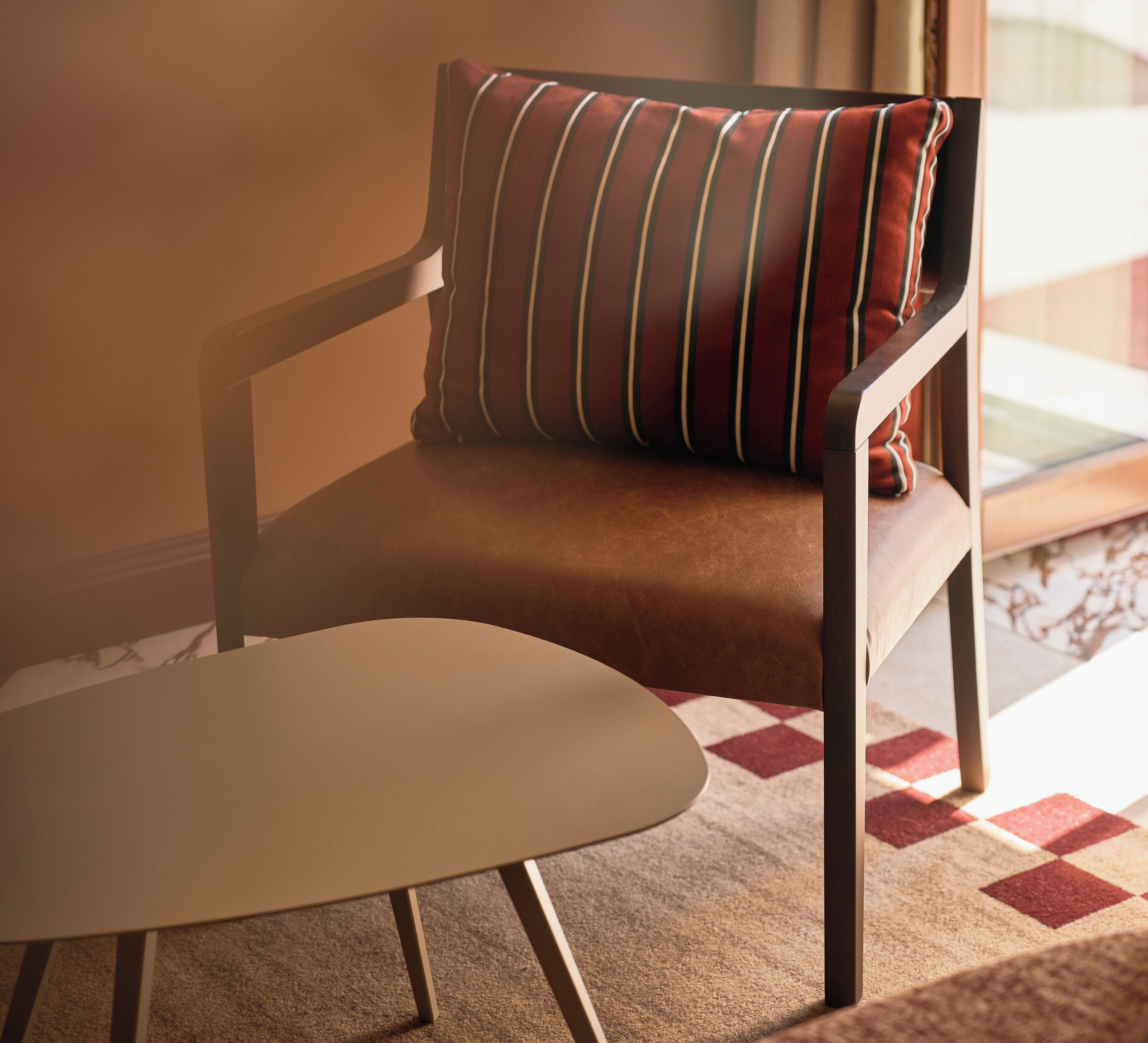 A chair with a cushion and a table in a room with a patterned carpet.