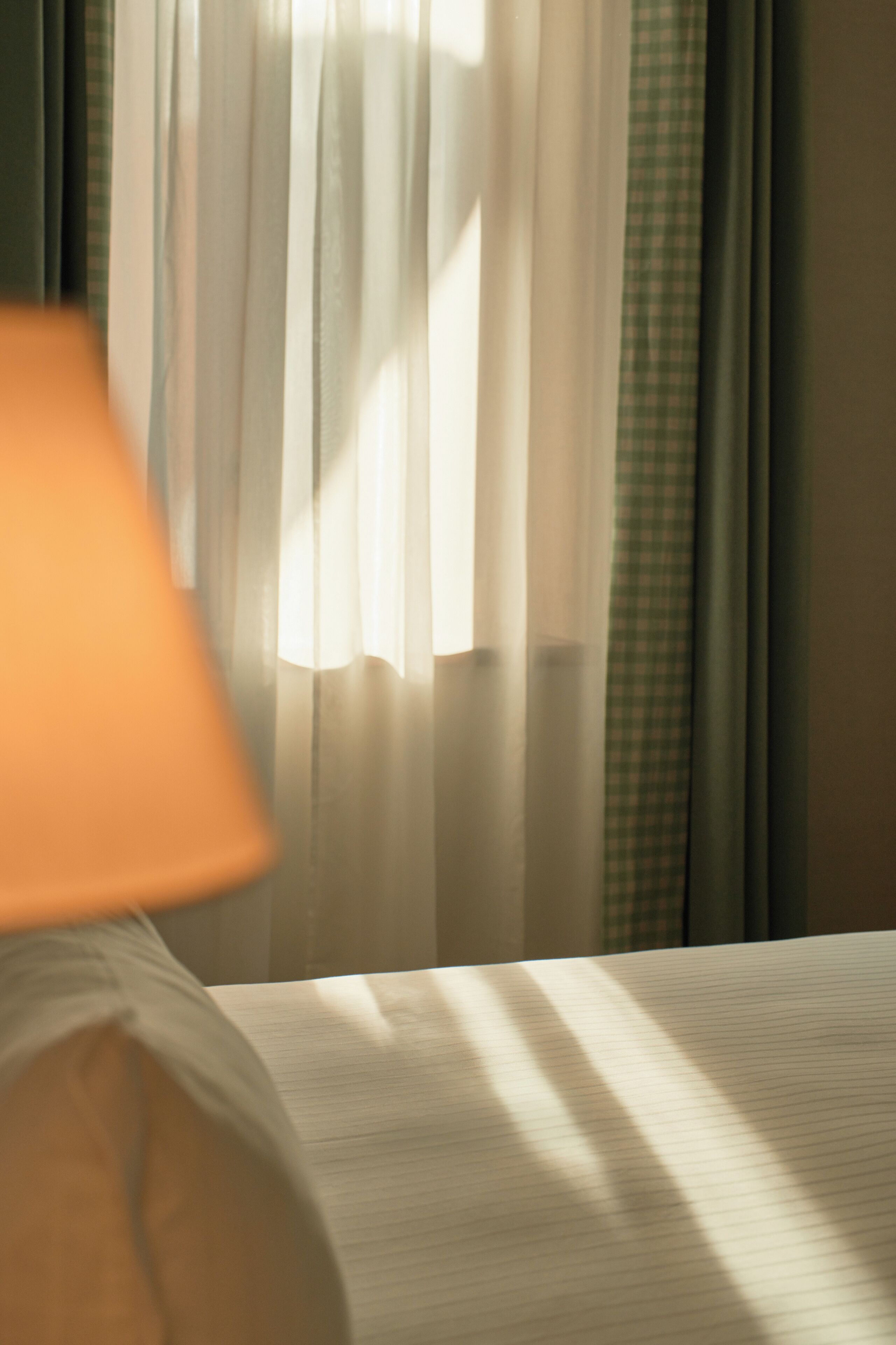 A room with a lamp, a window with sheer curtains, and a checkered curtain partially visible.