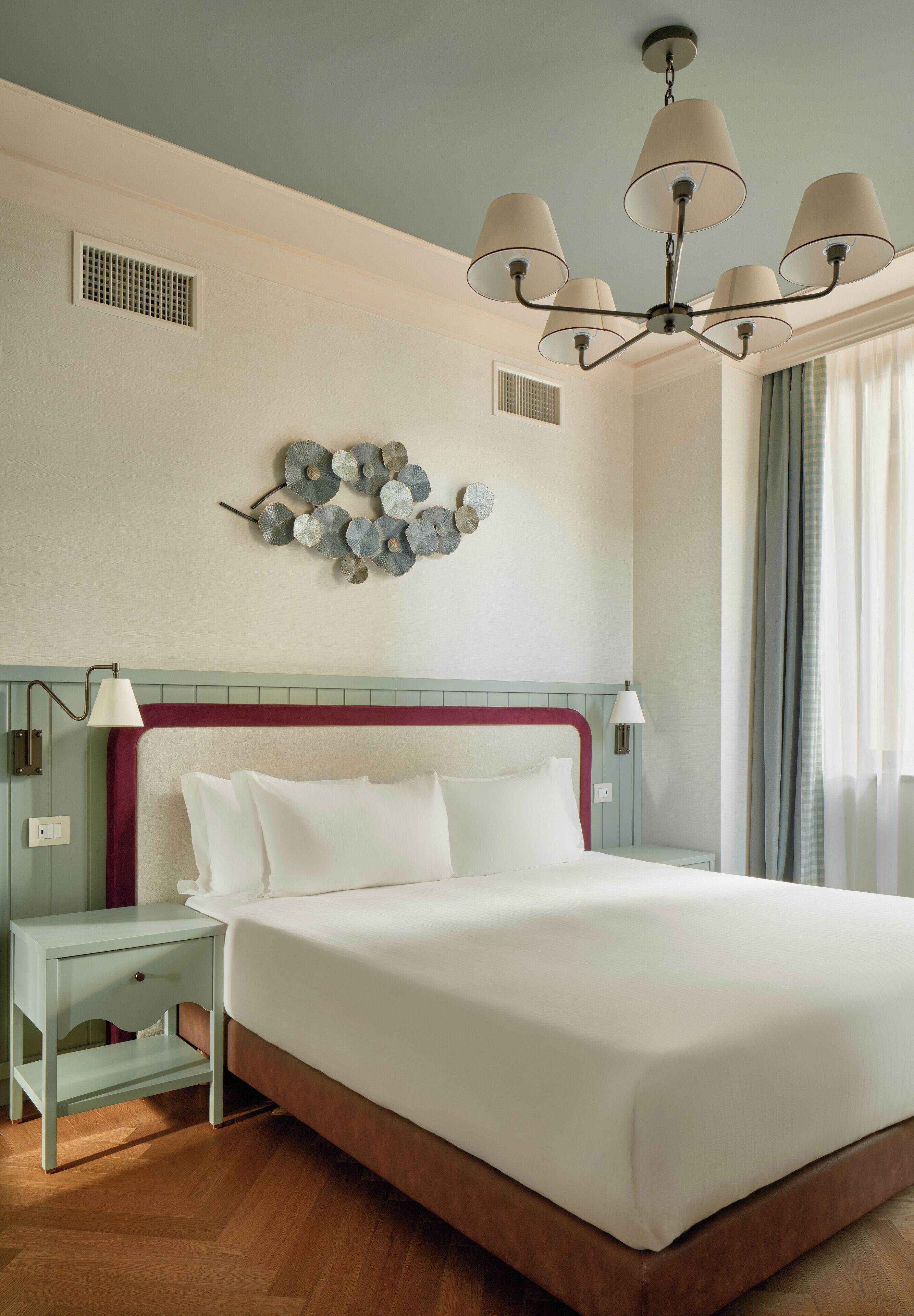 Une chambre d’hôtel avec un grand lit, un lustre, un élément décoratif mural et une table de chevet avec une lampe.