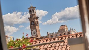 A balcony with terracotta tiles, a striped chair, and a view of a historic tower. - Homy Livia Verona (Verona)
