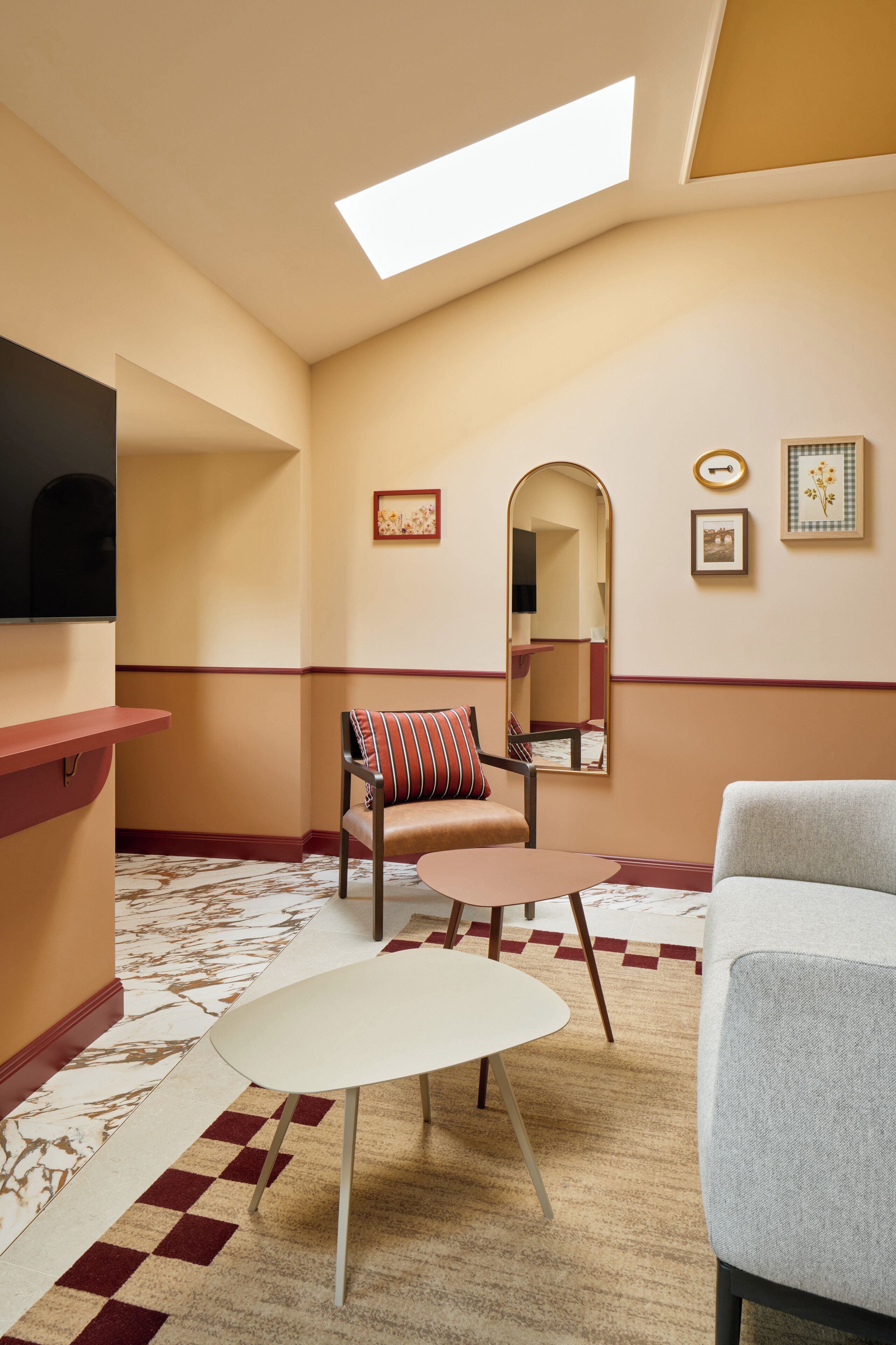A modern hotel room with a large window, a flat-screen TV, a dining table, a sofa, and a patterned carpet.
