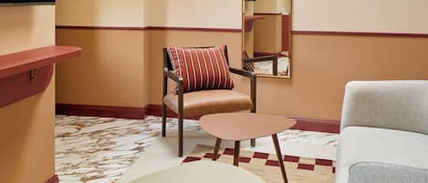 A modern hotel room with a large window, a flat-screen TV, a dining table, a sofa, and a patterned carpet.