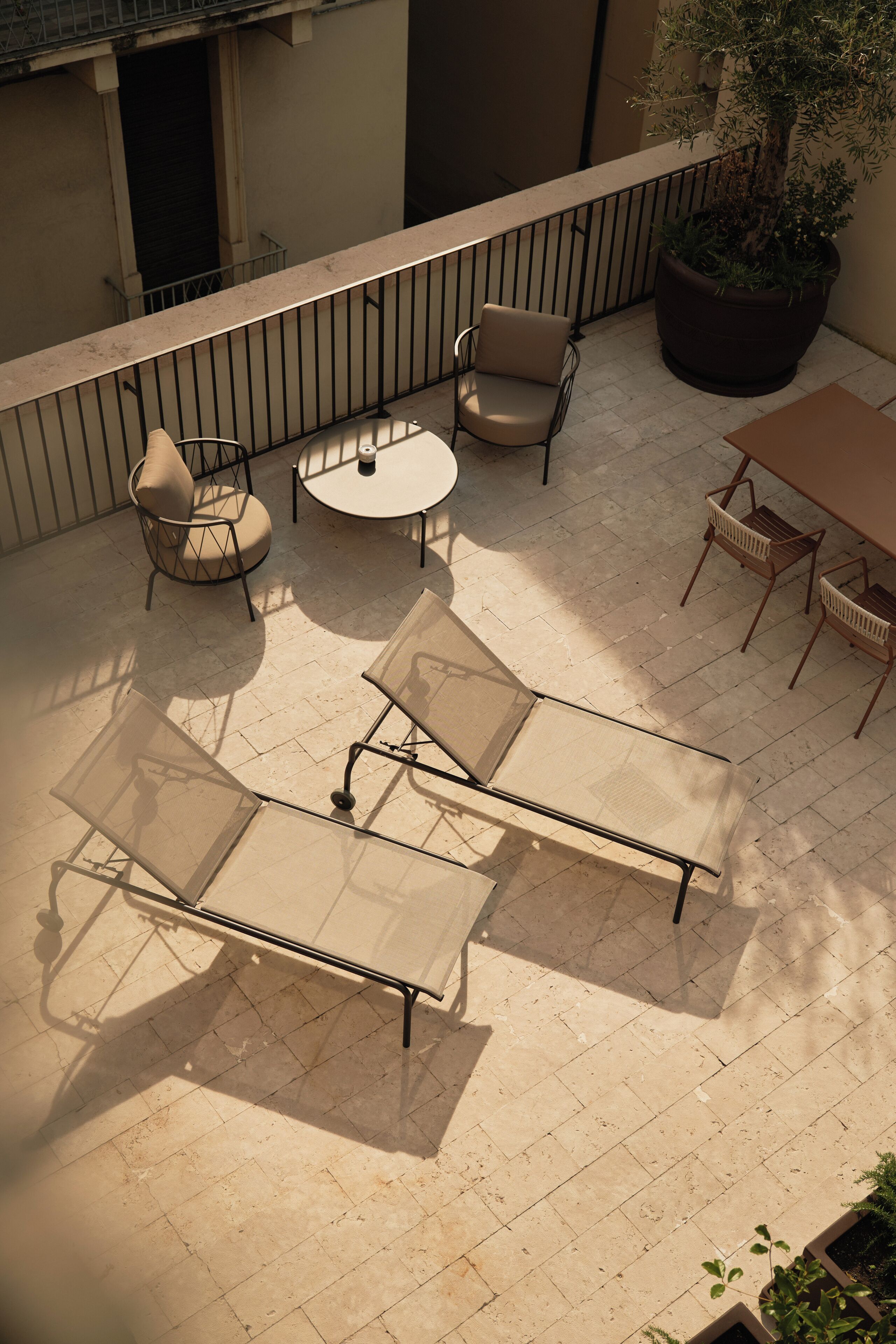 Patio esterno con un tavolo rotondo, due poltrone e un vaso con una pianta.