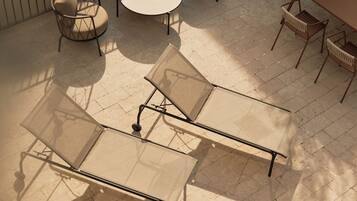 Un patio al aire libre con una mesa redonda, dos sillones de relax y una planta en maceta.