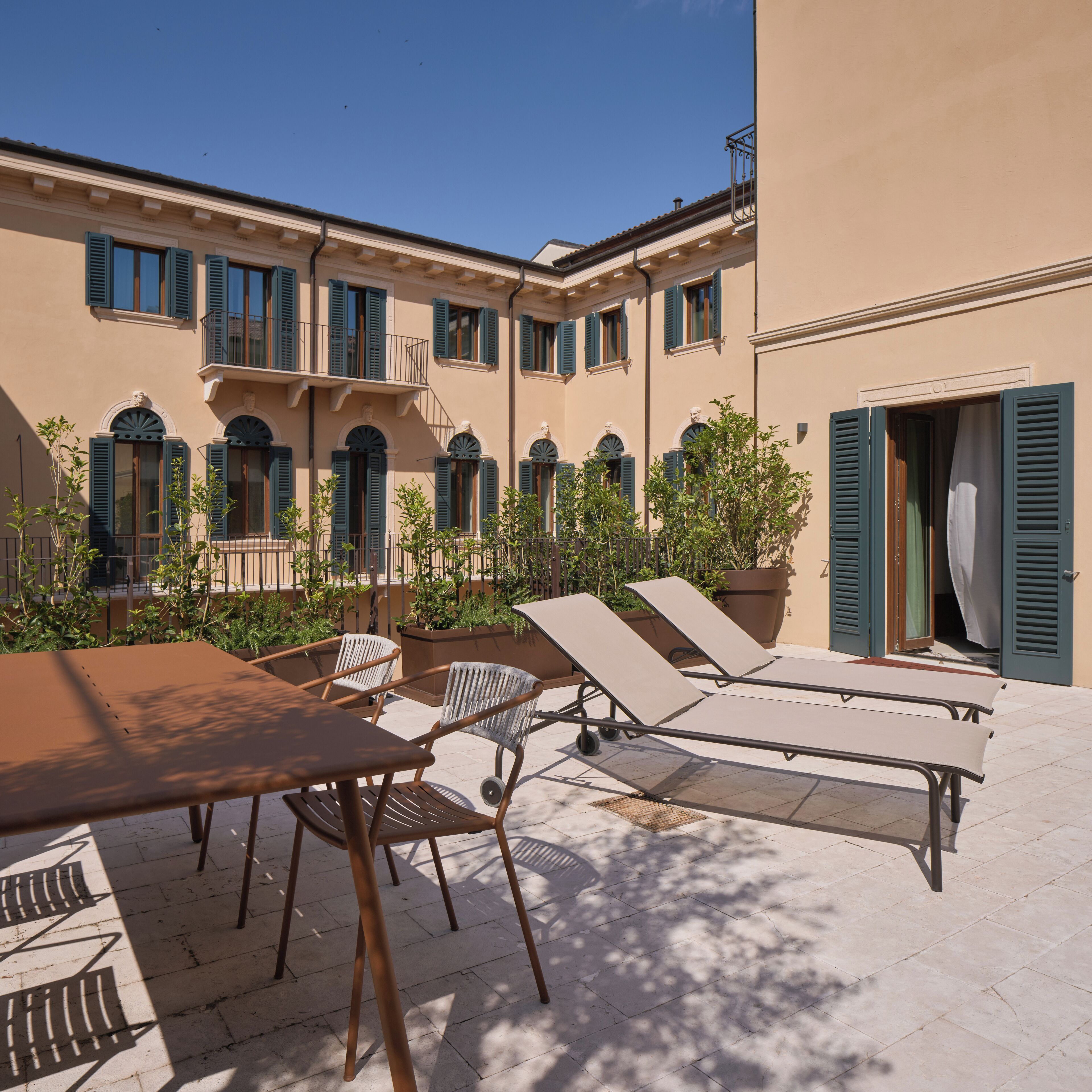 A courtyard with outdoor seating, a building with multiple windows and shutters, and a door.