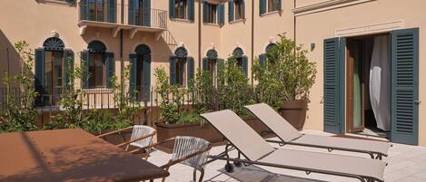 A courtyard with outdoor seating, a building with multiple windows and shutters, and a door.